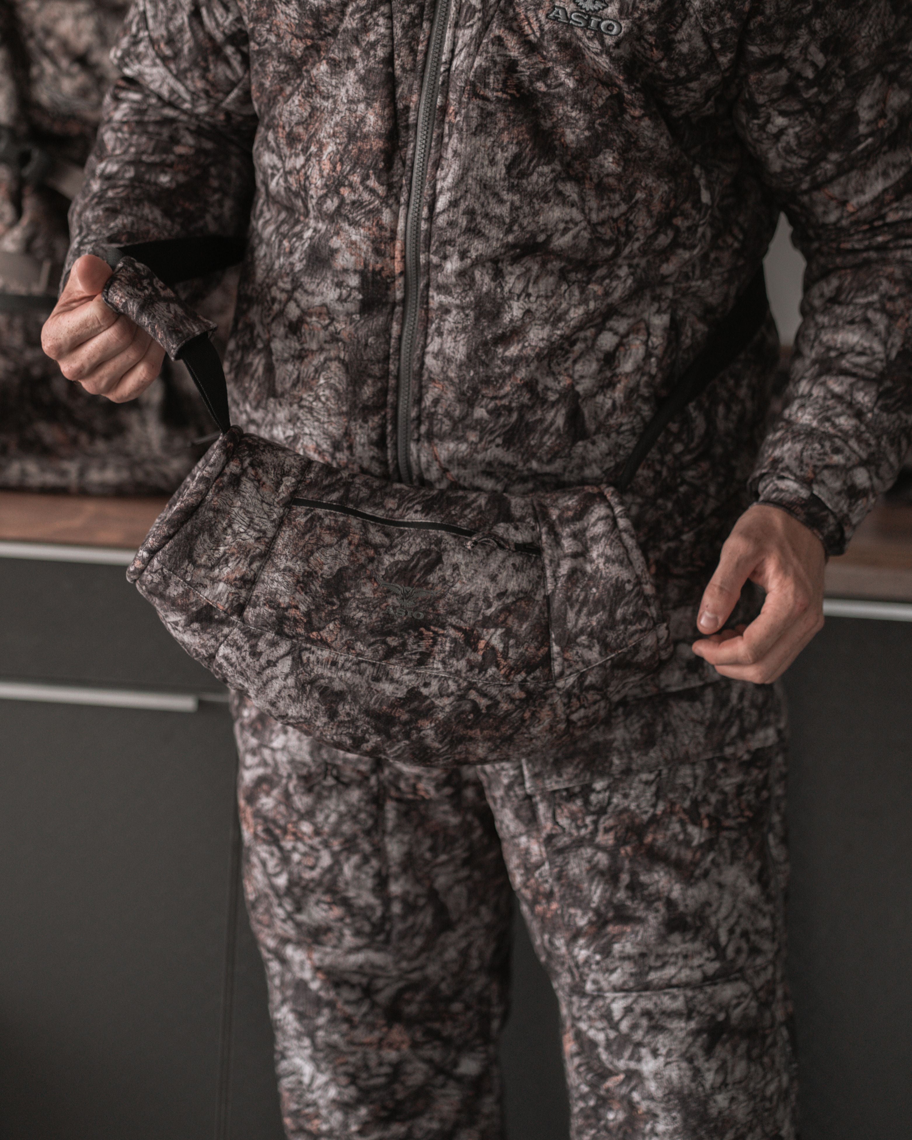 Hunter adjusting strap of ASIO Gear handmuff in Raptor camo, demonstrating secure fit and usability.