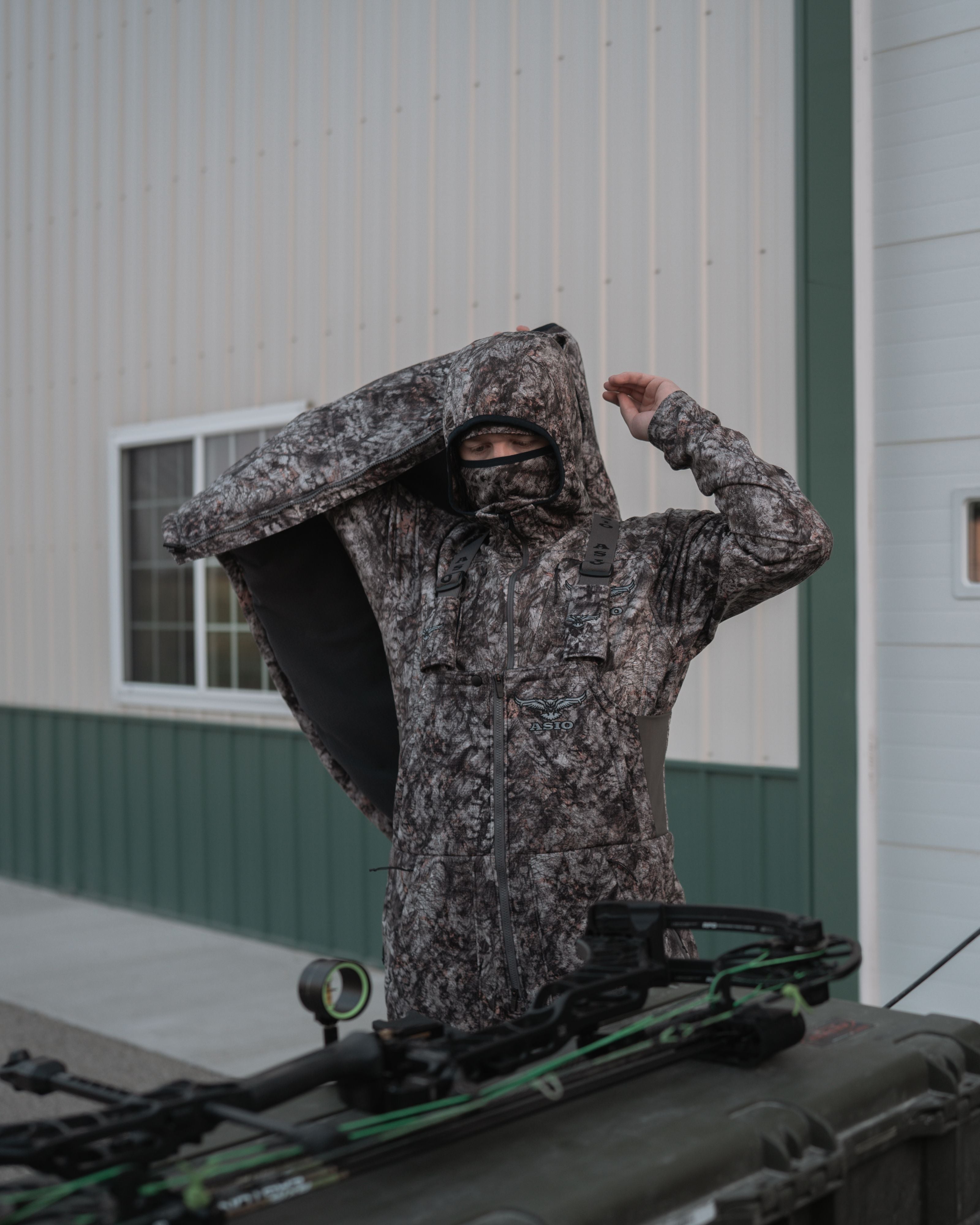 Treestand hunter adjusting ASIO Gear heavyweight vest in Raptor camo with bowhunting gear in foreground