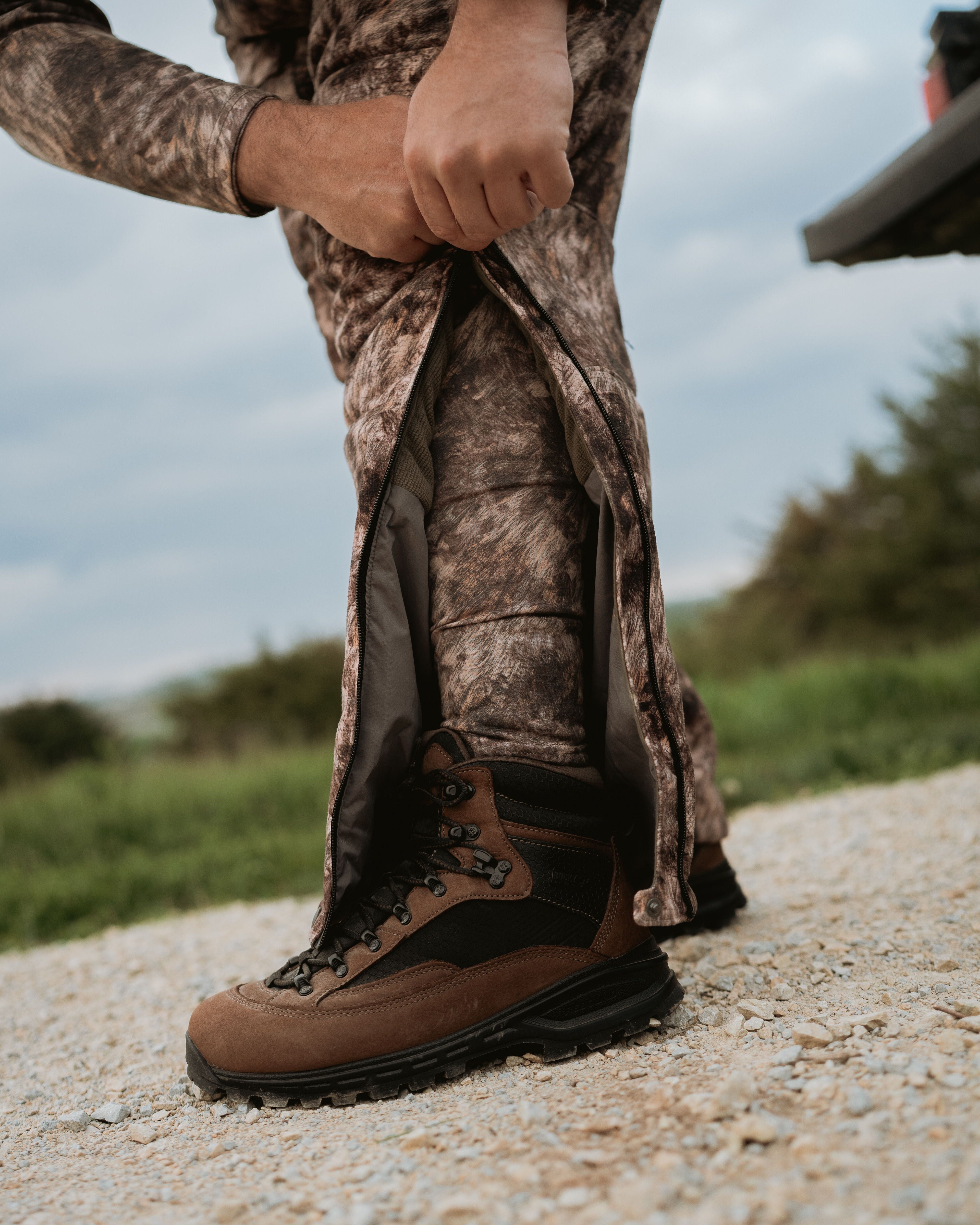 Hunter wearing ASIO Gear RAPX camo midweight baselayer while zipping bibs over boots in the field