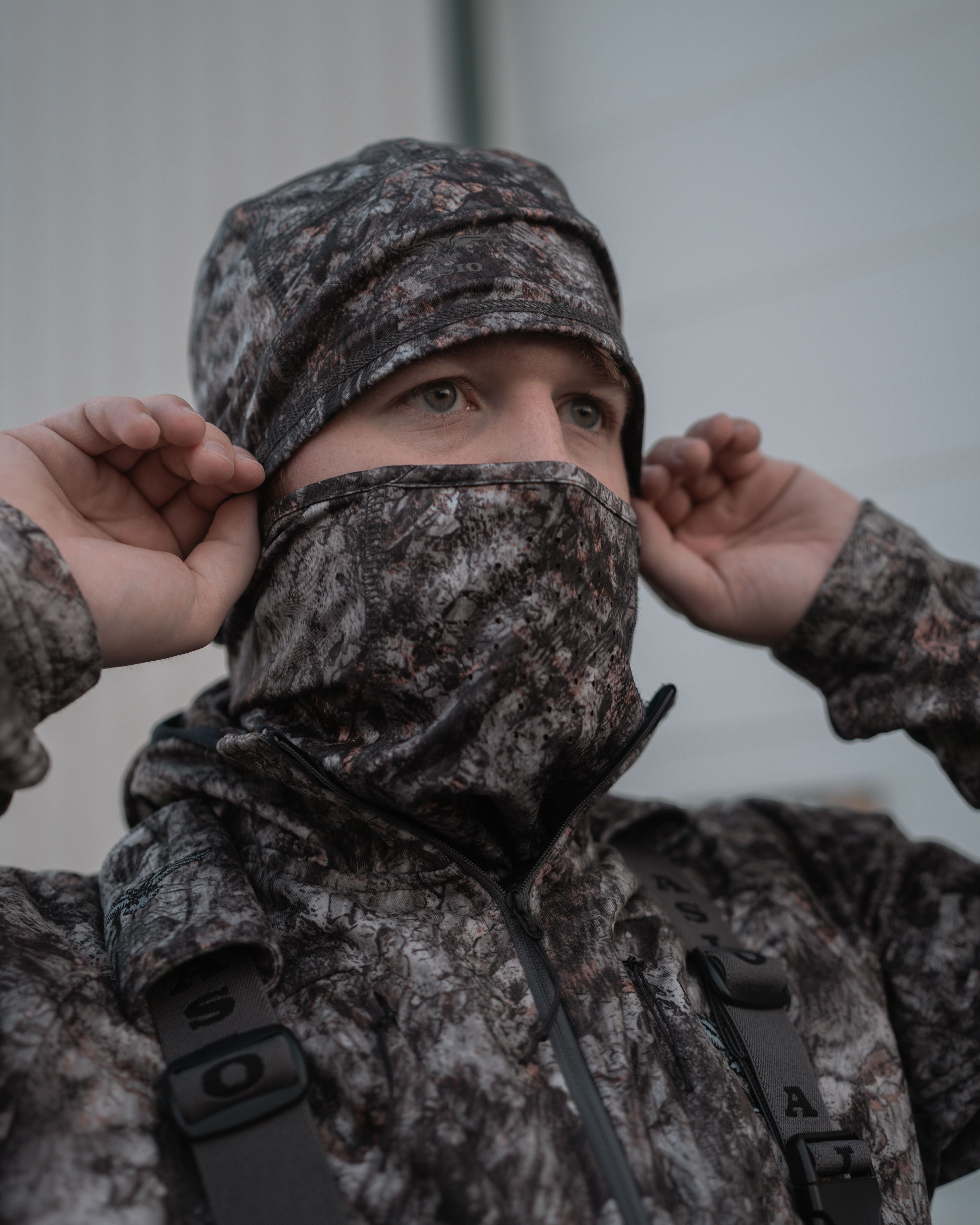 Hunter wearing ASIO Gear RAPTOR camo fleece-lined stretch beanie and face covering preparing for cold-weather bowhunt