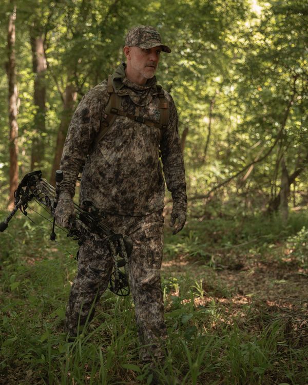 Bowhunter walking through hardwoods in full ASIO RAPX lightweight system during early season daylight entry