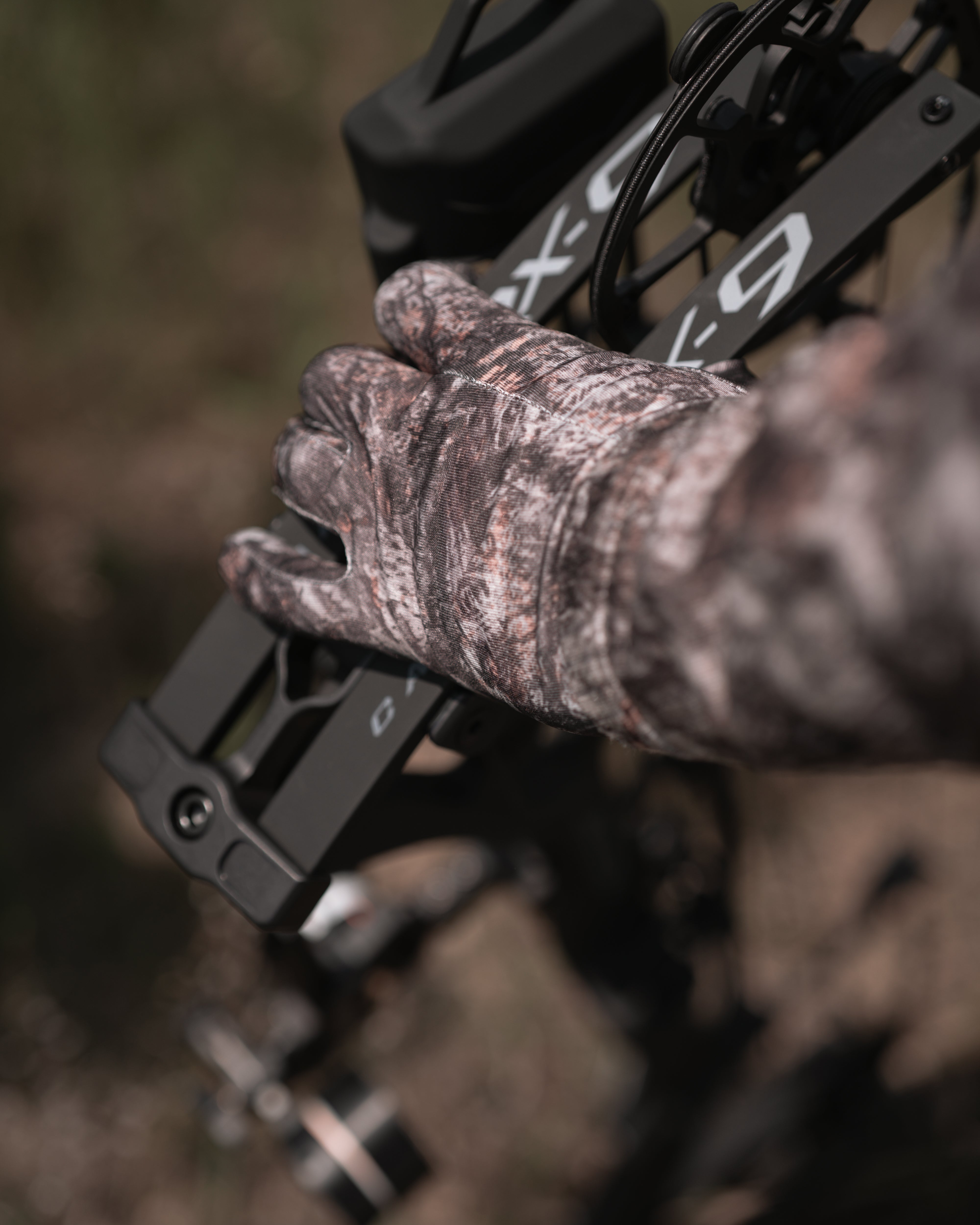 Hunter wearing RAPTOR camo lightweight stretch glove adjusting bow setup in sunlight