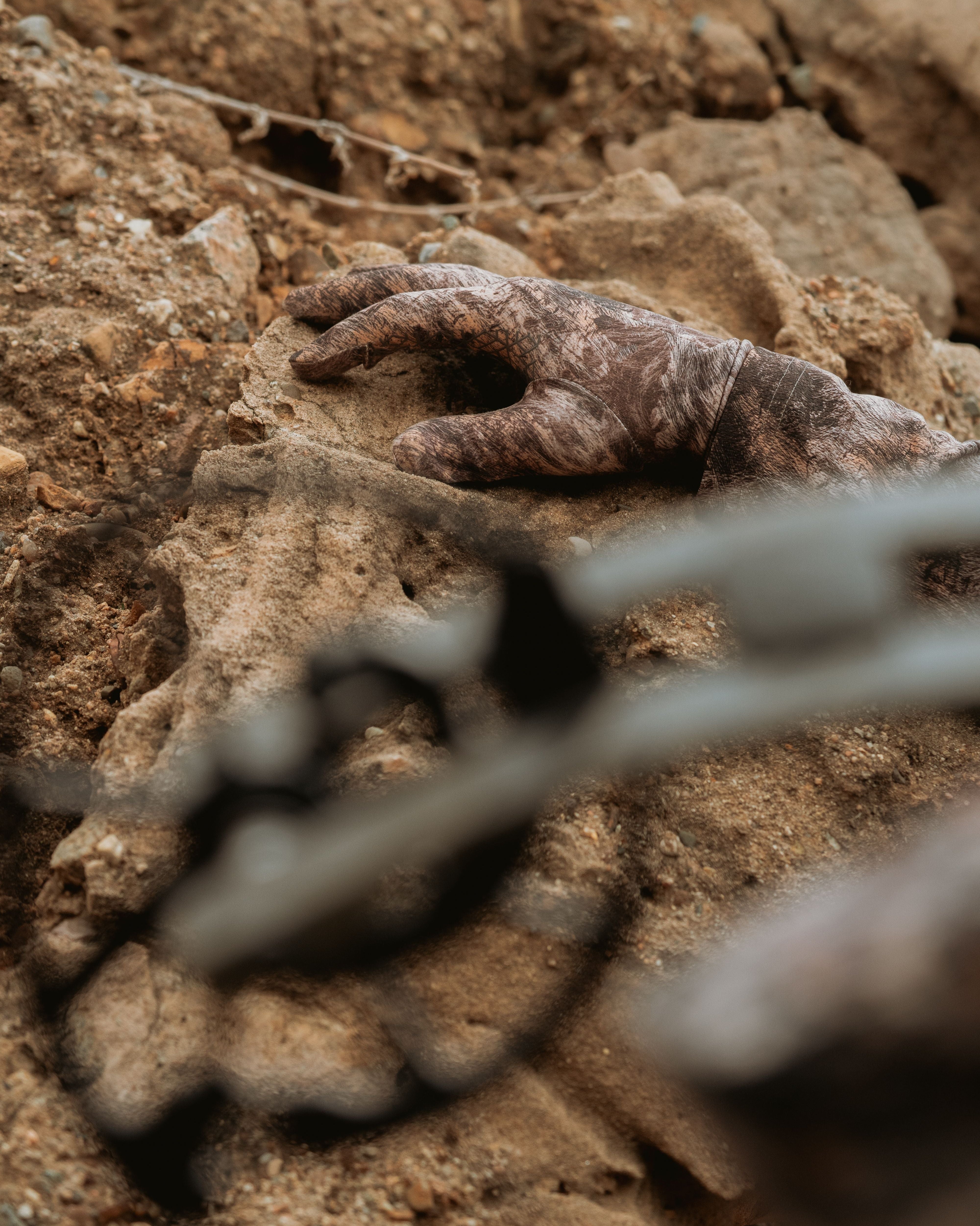 Close-up of ASIO Gear lightweight stretch glove in RAPTOR camo gripping rock during spot-and-stalk bowhunt