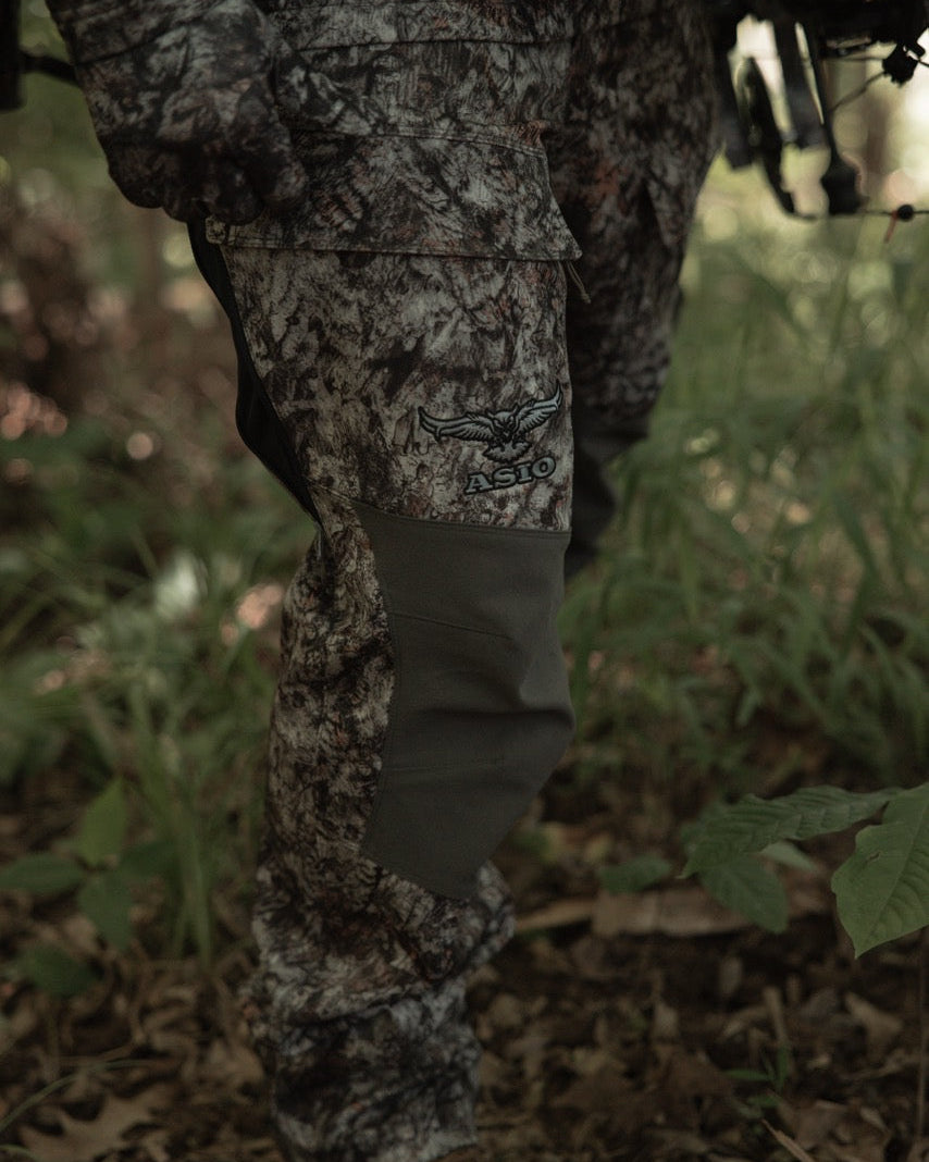 Hunter wearing ASIO Gear RAPTOR camo midweight bomb pant walking through brush during early season bowhunt
