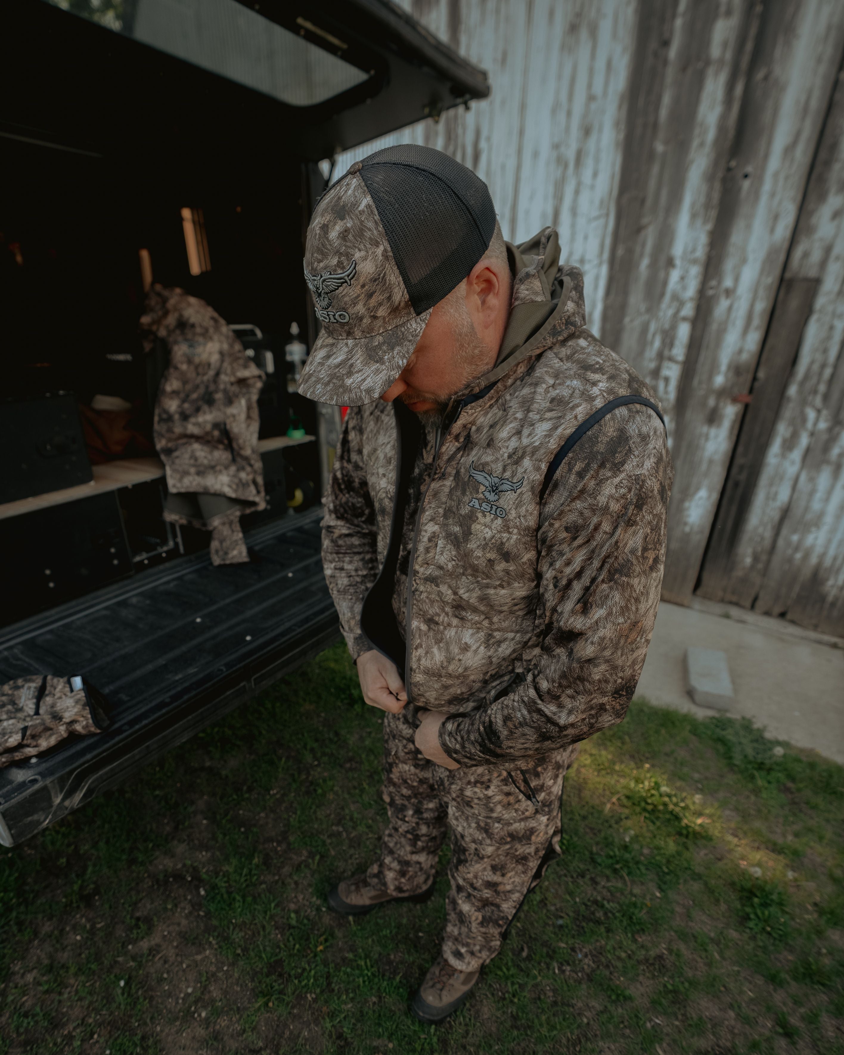 Hunter wearing ASIO Gear RAPX camo midweight puffy vest preparing gear at truck tailgate during mid season bowhunt