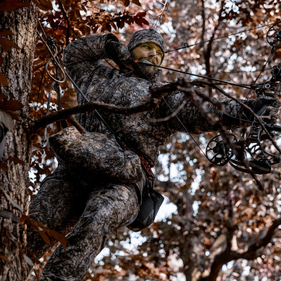 bowhunter wearing asio gear windproof hunting jacket with bow hunting collar in asio raptor camo while hunting whitetail deer